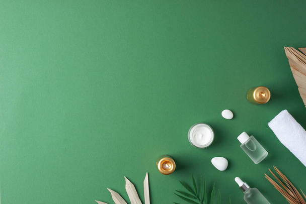 緑の背景に化粧品ボトル、キャンドル、ヤシの葉でスパトリートメント。平面、コピースペース - 写真・画像