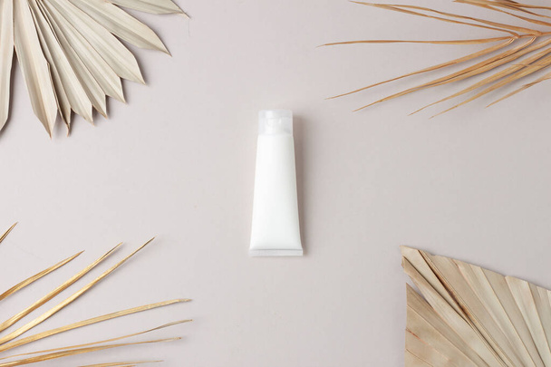 Белая тюбик косметического крема с пальмовым листом на сером фоне. Плоский лежал - Фото, изображение