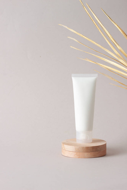 Tubo blanco de crema cosmética con podio de madera y hoja de palma sobre fondo gris. Cerrar, copiar espacio - Foto, imagen