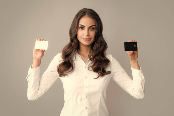 Portrét krásné ženy s potěšením a ukazující kreditní kartu, stojící nad šedým pozadím - Fotografie, Obrázek