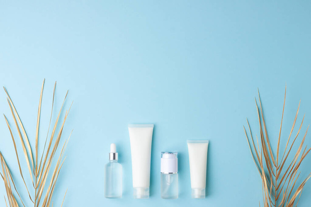 Cosmetische huidverzorgingsproducten met palmblad op blauwe achtergrond. Vlakke lay, kopieerruimte - Foto, afbeelding