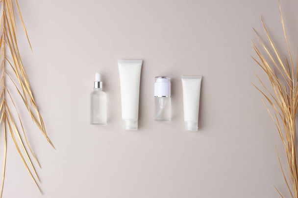 Productos cosméticos para el cuidado de la piel con hoja de palma sobre fondo gris. Colocación plana, espacio de copia - Foto, Imagen