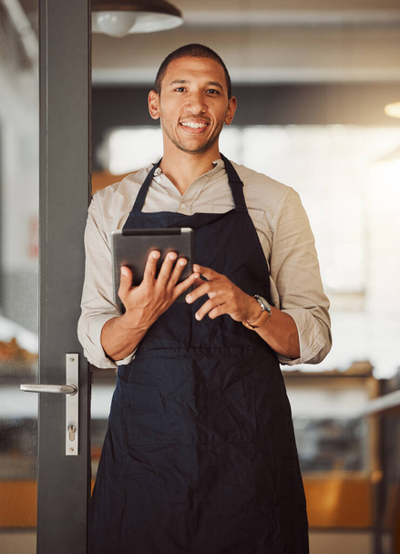 Businessman using a digital tablet in his cafe entrance. Bistro boss using an online app in the restaurant. Young small business owner using a wireless digital device in his cafe - Foto, immagini