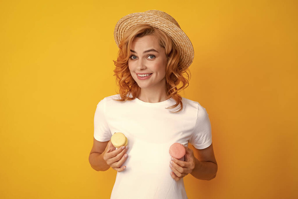 Roztomilá mladá žena drží makaróny. Krásná usmívající se mladá dívka jíst barevné makrónky přes žluté pozadí. Dieta, dietní koncept. - Fotografie, Obrázek