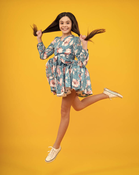 Täyspitkä ikionnellinen teini lapsi tyttö 12 13 14 vuotta hyppäämällä vanha eristetty keltaisella taustalla studio. Hassu hyppy. Lapsi kesällä liikkeen mekko - Valokuva, kuva