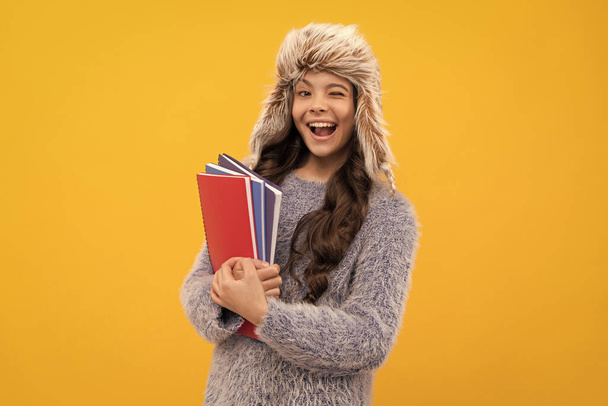 glücklich zwinkerndes Kind lange Haare in Hut mit Werbebuch auf gelbem Hintergrund, Wissen. - Foto, Bild