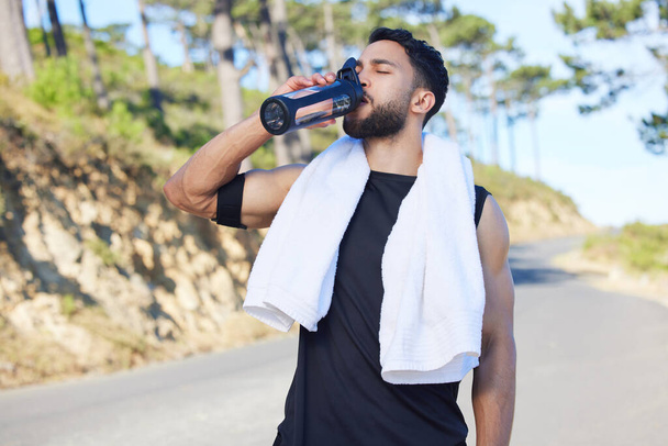 Water, fitness and exercise with a sports man drinking from a bottle for hydration during his workout or training routine. Health, wellness and rest with a male athlete taking a break from a routine. - Foto, immagini