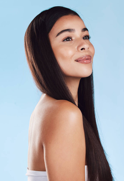 One beautiful young hispanic woman with healthy skin and sleek long hair smiling against a blue studio background. Happy mixed race model with flawless complexion and natural beauty. - Foto, Bild