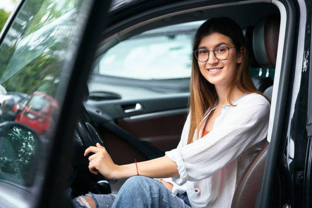Portrait of smiling confident woman driving new car, looking at camera. Transportation concept  - Фото, зображення
