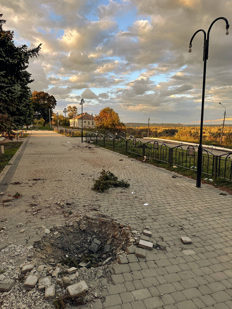 ウクライナの占領クピアンスクの町から解放された発射体からの爆弾被害を受けた通りとシェルクレーター。ロシアの砲撃の結果。戦争、ロシアの侵略と軍事犯罪の概念. - 写真・画像