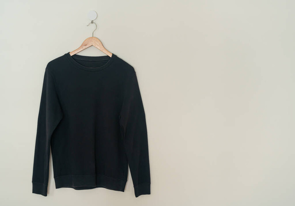 black sweater hanging with wood hanger on wall - Foto, Bild
