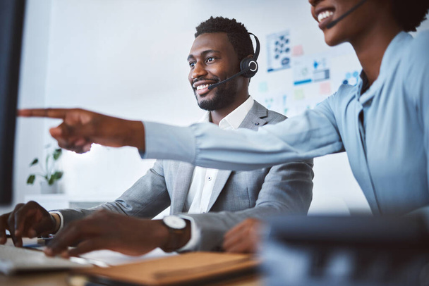 Szczęśliwy afrykański amerykański agent telemarketingu męskiego call center omawia plany z kolegą pracując razem nad komputerem w biurze. Rozwiązanie do rozwiązywania problemów dwóch konsultantów dla obsługi klienta. - Zdjęcie, obraz