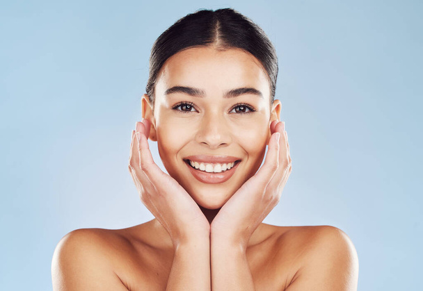 Closeup face beautiful young mixed race woman. Attractive female touching her face in studio isolated against a blue background. A skincare regime to keep your skin soft, smooth, glowing and healthy. - Zdjęcie, obraz