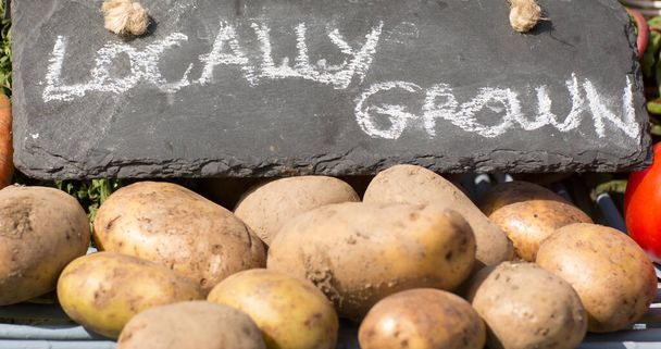 Close-up of locally grown text on stone with raw potatoes for sale at market stall. Unaltered, veganism, organic, food, healthy, business, support, vegan day and celebration concept. - Photo, Image