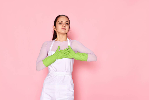 pretty friendly grateful woman in rubber gloves with hands on chest on pink background - Zdjęcie, obraz