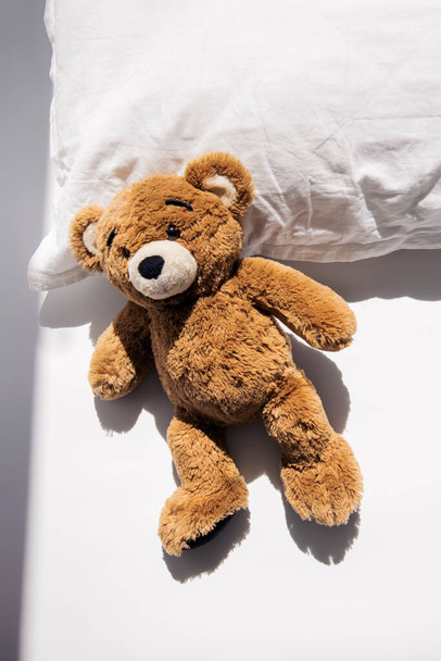 Мягкий игрушечный медведь лежит на подушке при естественном освещении. Вид сверху, плоский. - Фото, изображение