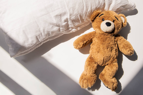 Мягкий игрушечный медведь лежит на подушке при естественном освещении. Вид сверху, плоский. - Фото, изображение