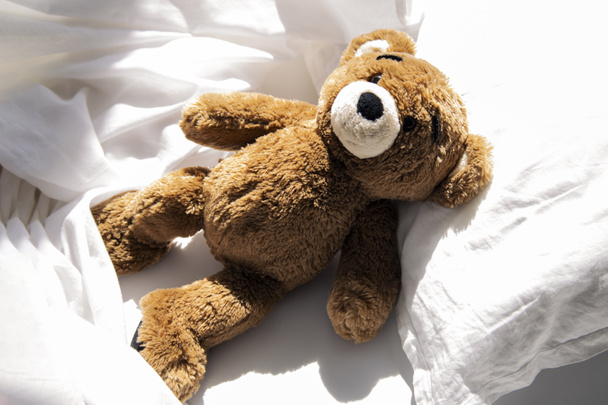 Morbido orso giocattolo per bambini si trova su un letto bianco. Vista dall'alto, piatta. - Foto, immagini