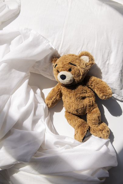 Мягкий игрушечный медведь лежит на кровати при естественном освещении. Вид сверху, плоский. - Фото, изображение