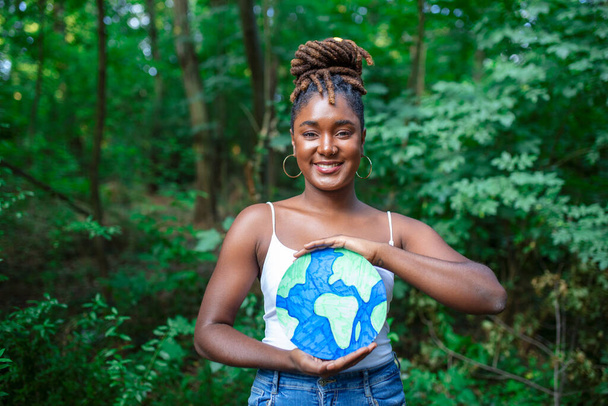 Африканська жінка - активістка, яка тримає в лісі плакат із планетарною землею.. - Фото, зображення