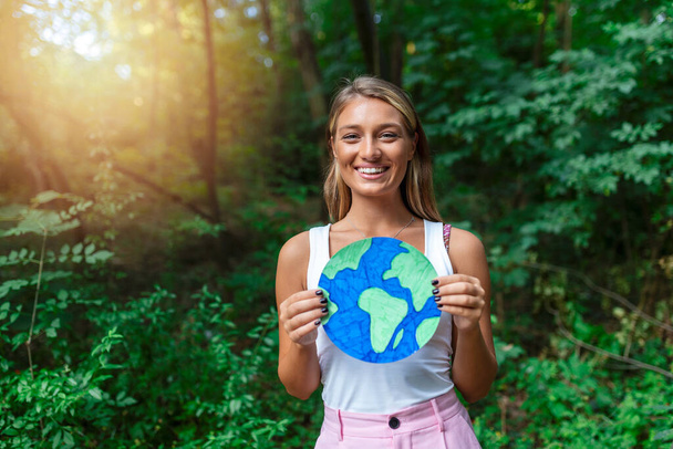 Женщина-активистка держит плакат планеты Земля в лесу, концепция загрязнения окружающей среды. - Фото, изображение