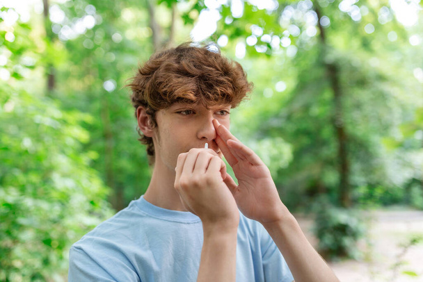 Młody człowiek używa aerozolu do nosa z powodu problemów z nosem i oddychaniem w parku publicznym. - Zdjęcie, obraz