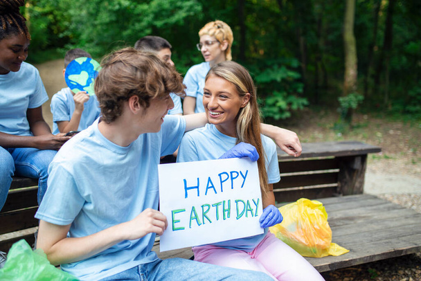 Mani femminili e maschili tengono un pezzo di cartone con le parole Happy Earth Day. Volontari felici e soddisfatti nella natura puliti e aiutano a mantenere l'ambiente. - Foto, immagini