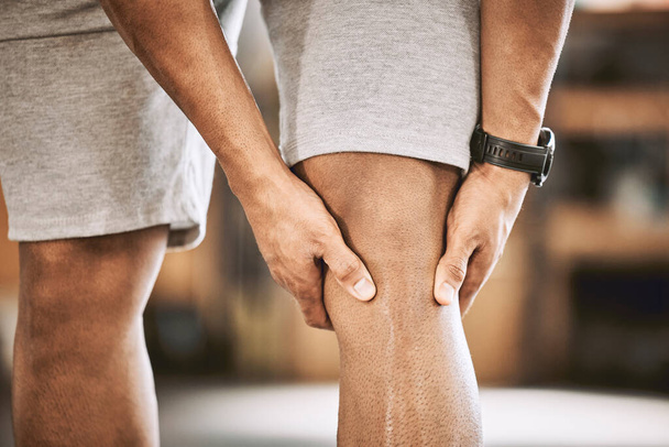 Closeup of fit man with a hurt knee. Hands of athlete holding a problem knee joint. Muscular bodybuilder with knee injury. Strong trainer with a knee muscle cramp. Exercise can be painful. - Photo, Image