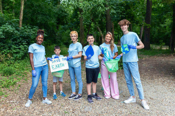 Vielfältige Gruppe von Menschen, die im freiwilligen gemeinnützigen Dienst im Park Müll sammeln. Glückliche internationale Freiwillige mit Plakat mit der Botschaft "Rettet die Erde". - Foto, Bild