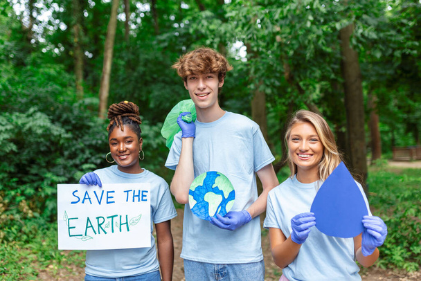 公園ボランティアコミュニティサービスでゴミを拾う多様な人々のグループ。「地球を救え」のメッセージを掲げた幸せな国際ボランティア. - 写真・画像