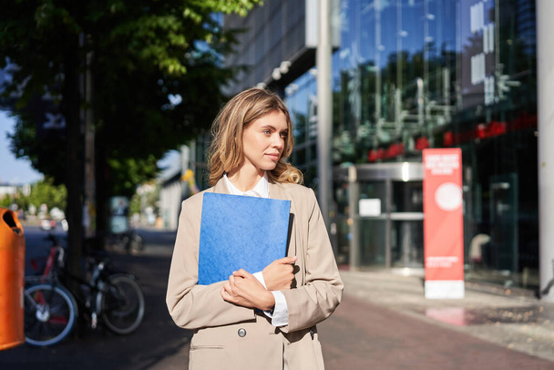 Δουλειά και εταιρικοί άνθρωποι. Αυτοπεποίθηση επιχειρηματίας κρατώντας ένα μπλε φάκελο με έγγραφα των επιχειρήσεων, το περπάτημα στο δρόμο. - Φωτογραφία, εικόνα
