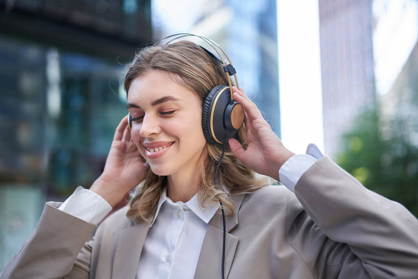 Gelukkige zakenvrouw glimlachend, muziek luisterend in koptelefoon terwijl buiten op straat. - Foto, afbeelding