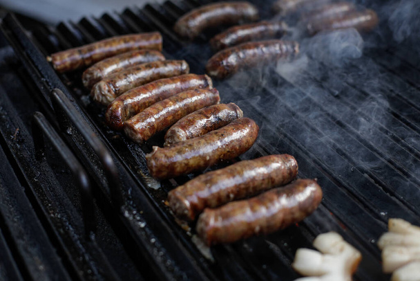 Мелкая глубина резкости (выборочная фокусировка) детали со свиными колбасами, приготовленными на гриле для барбекю, на европейском фермерском рынке. - Фото, изображение