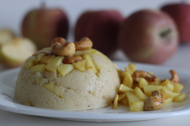 Almás Sheera. Indiai puding darált lisztből, ghee-ből, tejből, datolyából és száraz gyümölcsből, karamellizált almával tálalva. Klasszikus indiai édes lövés fehér háttér mellett friss piros alma - Fotó, kép