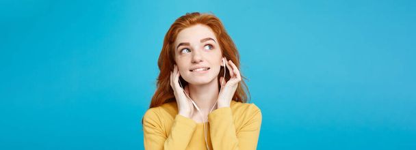 Lifestyle concept - Portrait of cheerful happy ginger red hair girl enjoy listening to music with headphones joyful smiling to camera. Isolated on Blue Pastel Background. Copy space - Fotó, kép