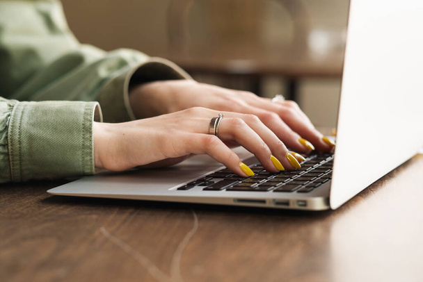 Gros plan d'une femme méconnaissable travaillant sur un ordinateur portable à une table basse, étudiante utilisant son carnet pour étudier au café - Photo, image
