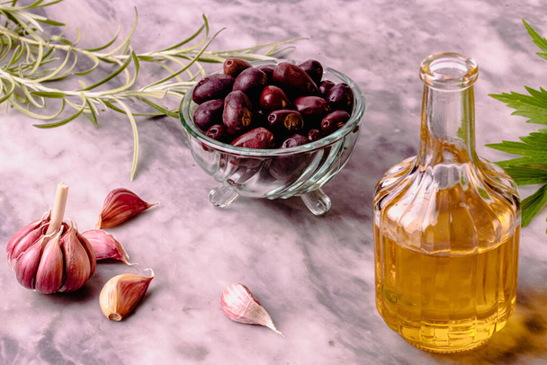 Верхний вид оливкового масла, чеснока и свежих, зеленых ароматических любовных и розмариновых листьев на мраморном столе. - Фото, изображение