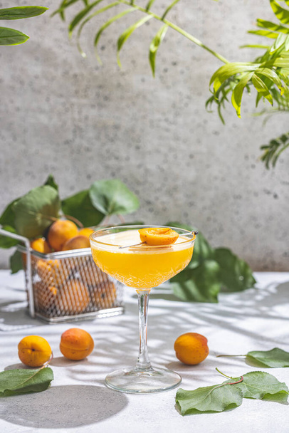 Элегантный стакан абрикосового коктейля Lady Cocktail или коктейли в окружении ингредиентов и свежих фруктов на серой поверхности стола, готовых к употреблению - Фото, изображение