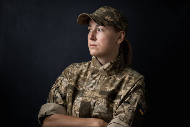 Retrato de una hermosa chica con bandera ucraniana amarilla y azul en su mejilla con uniforme militar. Mujeres ucranianas en el ejército. Fondo negro. Apoyar a Ucrania - Foto, Imagen