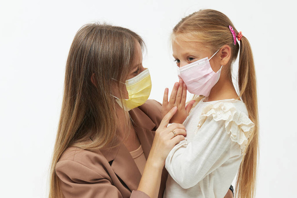 Caring for loved ones. Young mother hugs little daughter in protective medical masks during Covid-19 pandemics. Studio white background - Foto, immagini