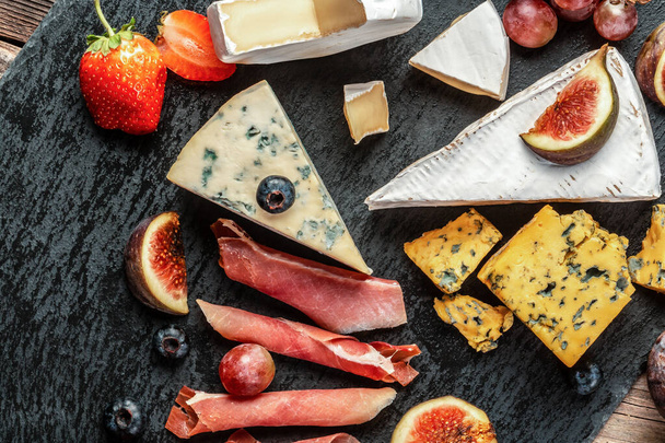 Vários tipos de queijo, peças tradicionais de queijo manchego francês, italiano e espanhol com uvas e figos servidos em mesa de madeira. - Foto, Imagem