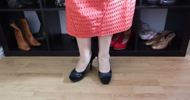 Samičí nohy a nohy stojící dospělé ženy zkoušející si černé vysoké podpatky, domácí šatna s botou, oranžové šaty, výhled z boku. Krása, půvab a módní koncept - Záběry, video