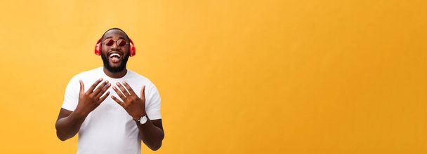 schöner junger afrikanisch-amerikanischer Mann, der Musik auf seinem mobilen Gerät hört und lächelt. isoliert über gelbem Hintergrund - Foto, Bild