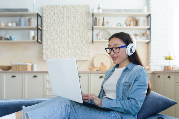 Donna asiatica seduta sul divano a casa usando il computer portatile per guardare video educativi, studente che studia in remoto online. - Foto, immagini