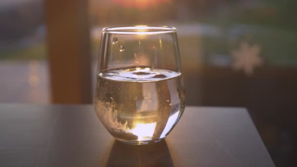 SLOW MOTION, CLOSE UP: Oplossende bruistablet gedropt in een drinkglas met achtergrondverlichting en de gouden ondergaande zon. Sprankelende drank om weer gezond te worden. Thuisbehandeling voor seizoensziekten. - Video