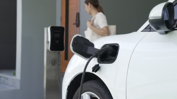 A woman unplugs the electric vehicles charger at his residence. Concept of the use of electric vehicles in a progressive lifestyle contributes to a clean and healthy environment. - Footage, Video