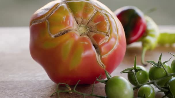 Parte superior agrietada de tomate maduro rodeado de verduras y un montón de tomates cherry verdes en la superficie de madera - Metraje, vídeo