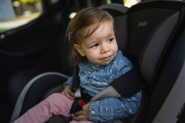 One girl small caucasian toddler female child sitting in the safety car seat chair 18 months old transportation concept copy space - Photo, Image
