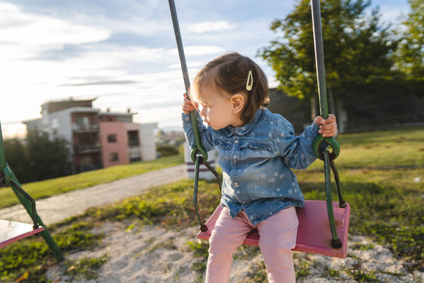 Une fille petit enfant caucasien femelle tout-petit 18 mois s'amuser dans le parc sur la balançoire balançant seul dans l'enfance de jour et grandir concept copier l'espace - Photo, image