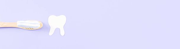 Bamboe tandenborstel met tandpasta en papieren tand aan de rechterkant tegen een zachte lila achtergrond met kopieerruimte aan de rechterkant, close-up bovenaanzicht. - Foto, afbeelding